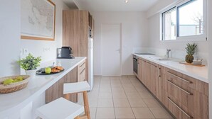 Een moderne keuken met witte aanrechtbladen, houten kastjes en een groot raam dat voor natuurlijk licht zorgt.