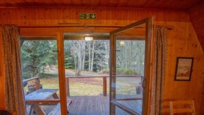 A wooden cabin with a glass door leading to an outdoor deck with picnic tables.