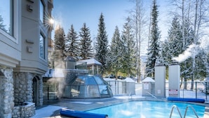 A pool area with a glass-enclosed structure, stone walls, and snow-covered trees.