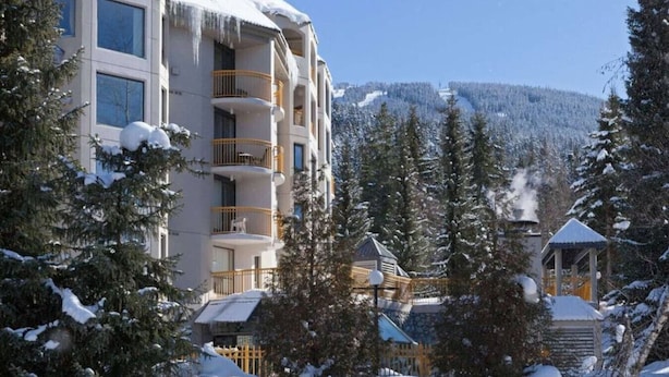 A multi-story hotel with balconies, surrounded by snow-covered trees and a mountain in the background.