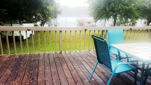 A wooden deck with a table and chairs, surrounded by a white fence and trees.