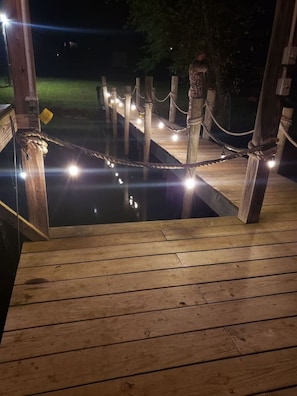 Un muelle de madera con una barandilla de cuerda y luces, que conduce a una masa de agua.