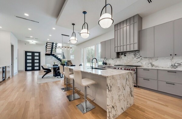 A modern kitchen with a marble island, stainless steel appliances, and pendant lighting.