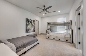 A bedroom with a bunk bed, a single bed, a ceiling fan, and a painting on the wall.