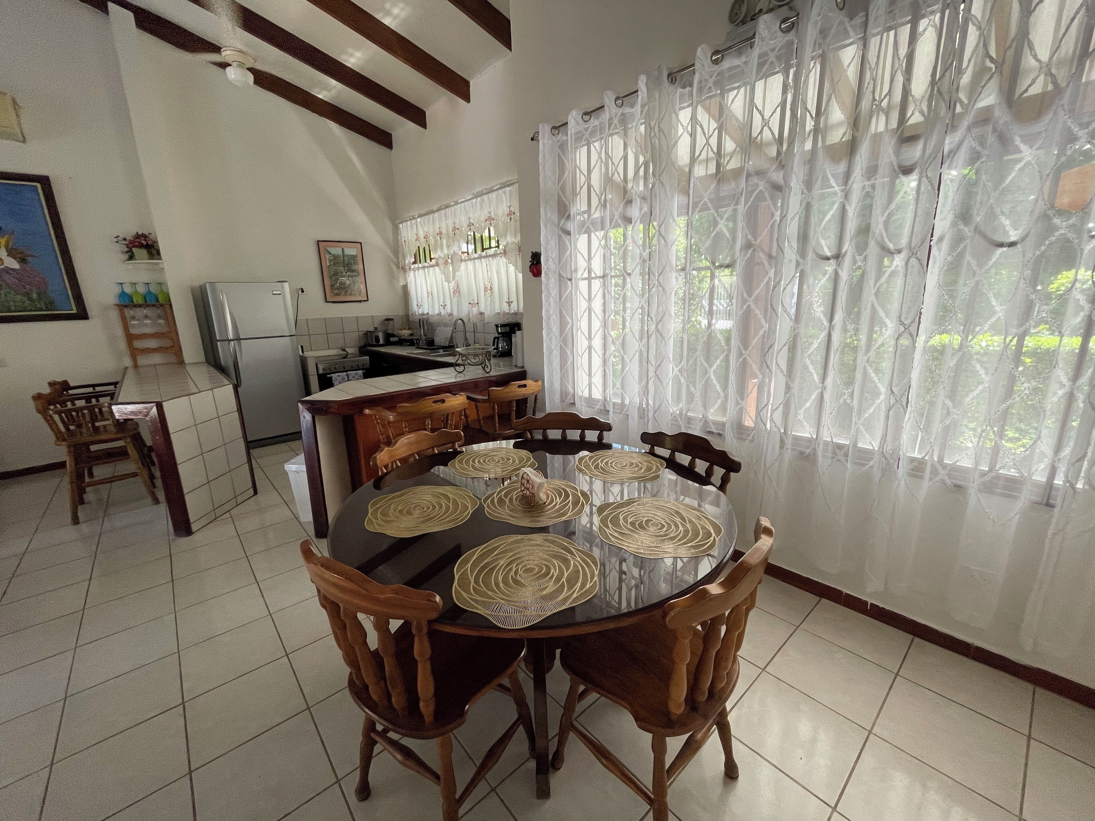 A dining area with a round table, wooden chairs, and a kitchen in the background.