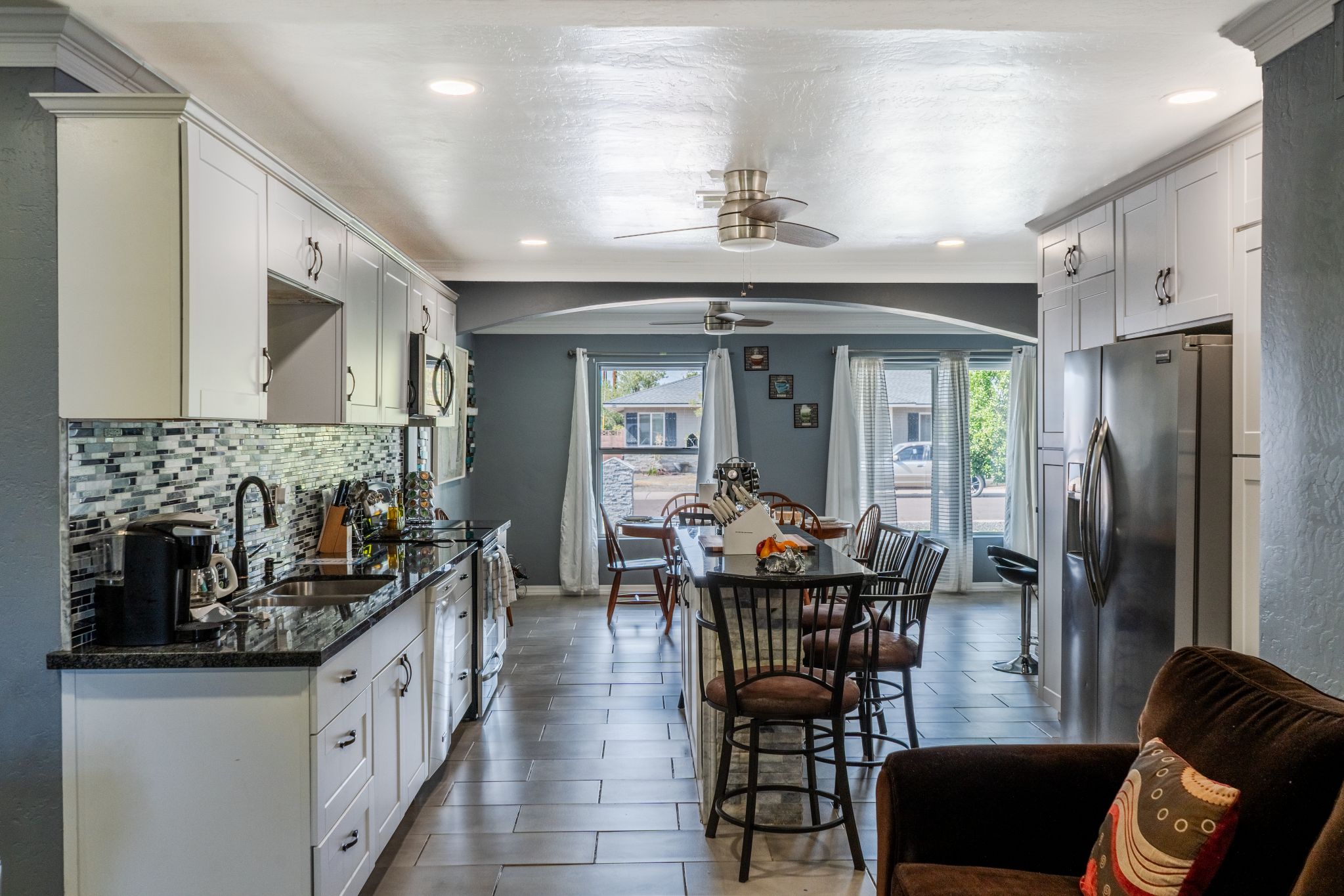 A modern kitchen with a dining area, featuring a large island, stainless steel appliances, and a ceiling fan.