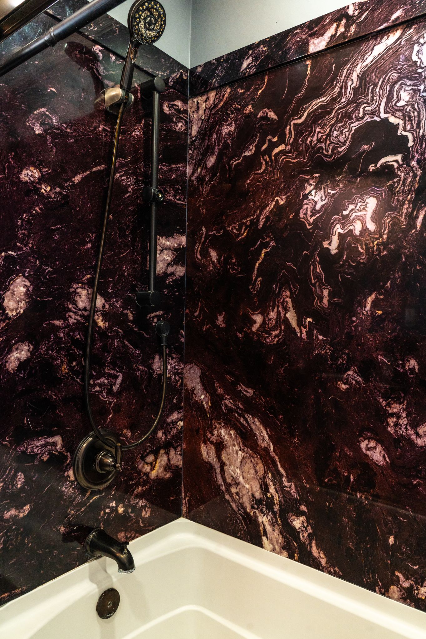 Une salle de bain avec une baignoire, une douche équipée d’un pommeau de douche à main et des murs en marbre.