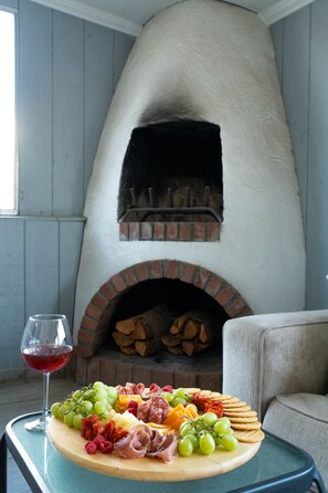 Une pièce avec une cheminée en briques, une table sur laquelle est disposé un plateau de fromages et de fruits, et un verre de vin rouge.