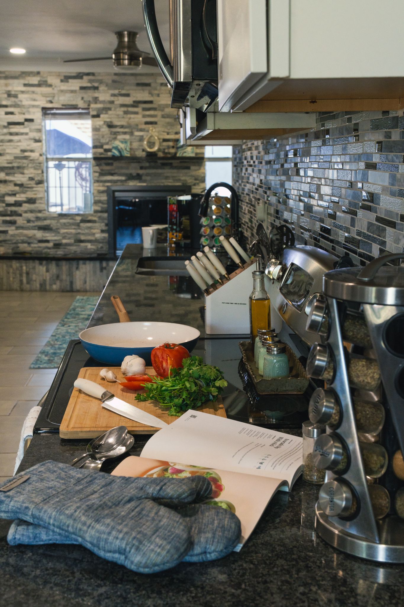 Una cucina moderna con un piano di lavoro in granito, elettrodomestici in acciaio inossidabile e una parete di piccole piastrelle.