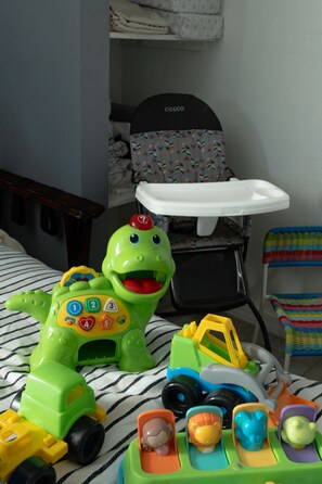 Un espace de jeux pour enfants avec un lit, un berceau et divers jouets, notamment un dinosaure vert et un camion jouet.