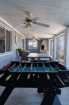 Une pièce avec une table de baby-foot, des ventilateurs de plafond et une fenêtre donnant sur un beau paysage.