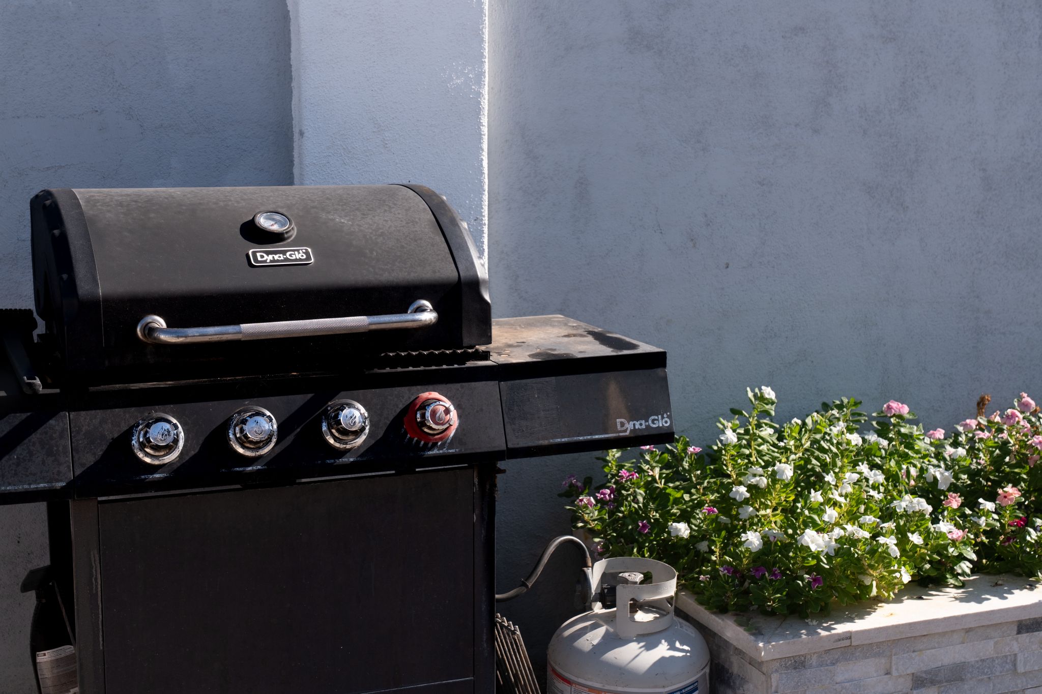 Een zwarte buitenbarbecue met 'Dyna-Glo' branding, vier bedieningsknoppen en een metalen handgreep.