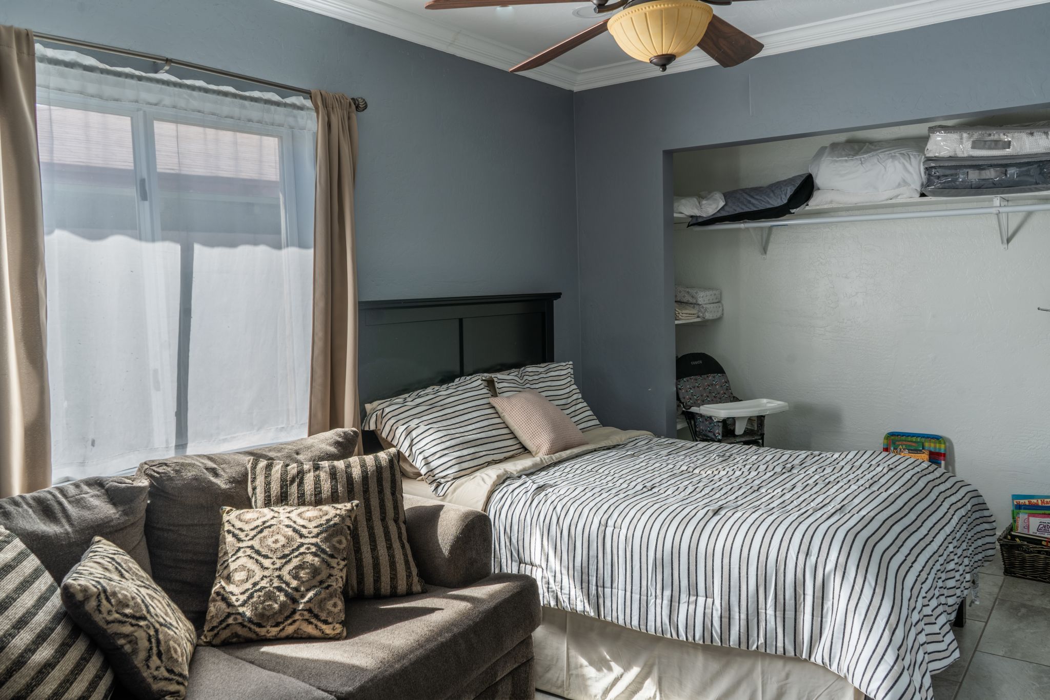 A bedroom with a bed, a sofa, a ceiling fan, and a window with curtains.