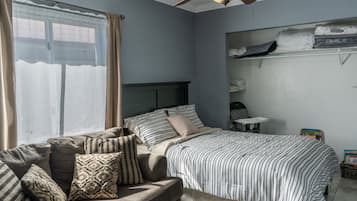 A bedroom with a bed, a sofa, a ceiling fan, and a window with curtains.