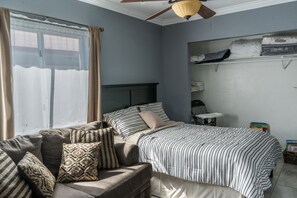 Un dormitorio con cama, sofá, ventilador de techo y ventana con cortinas.