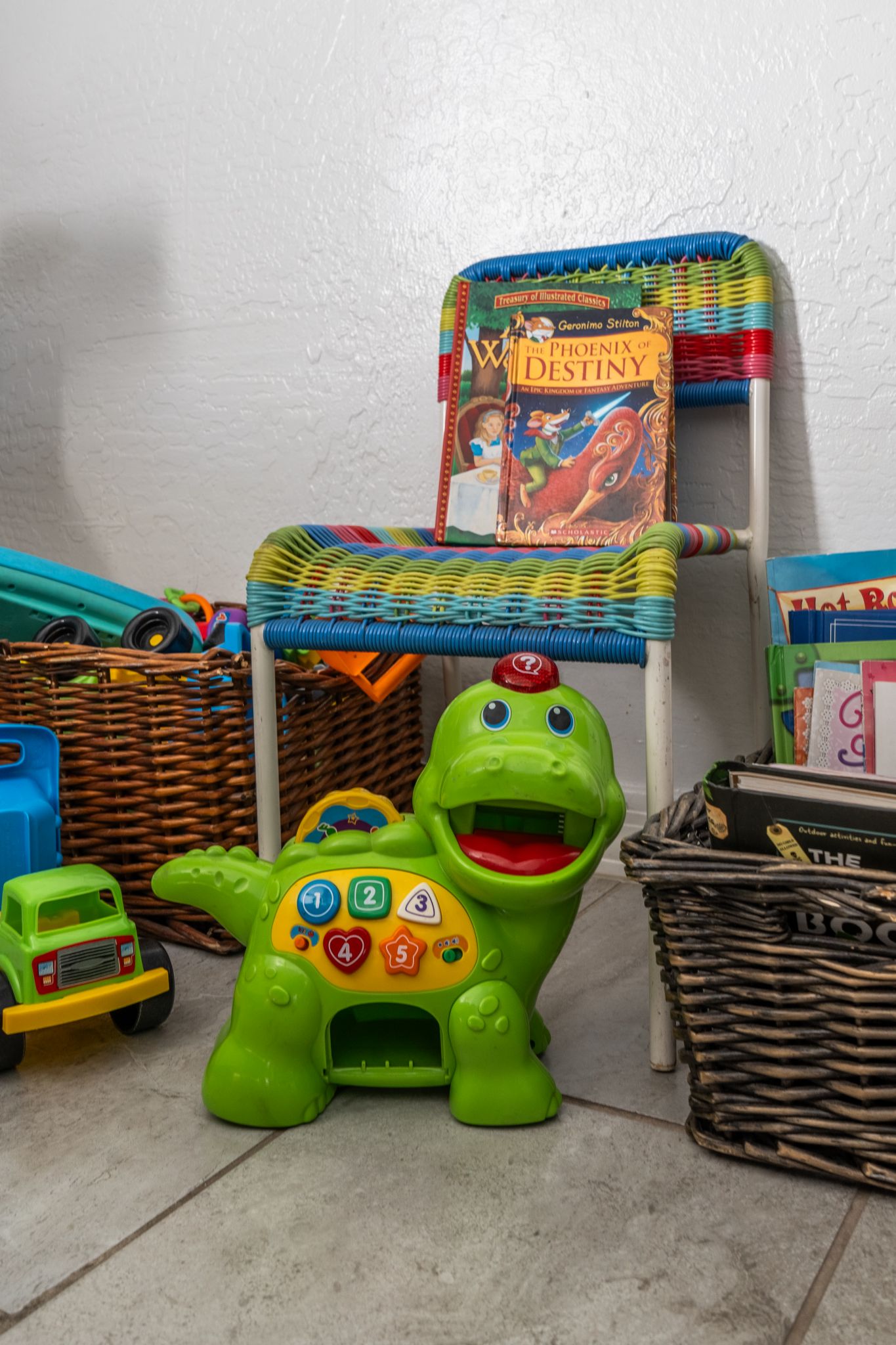 Un dinosaurio de juguete verde con un panel de control y una silla de mimbre con un libro colorido.