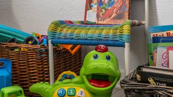 Un dinosaurio de juguete verde con un panel de control y una silla de mimbre con un libro colorido.