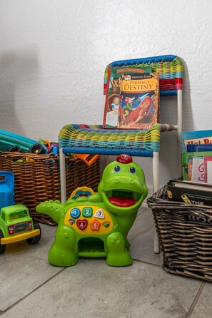 Un dinosaurio de juguete verde con un panel de control y una silla de mimbre con un libro colorido.