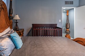 Ein Schlafzimmer mit Bett, Nachttisch, Lampe, Babybett und einem dekorativen Holz-Kopfteil.