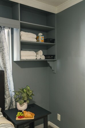 Une pièce avec un mur gris, une étagère avec des serviettes pliées, une boîte de mouchoirs et une plante en pot sur une petite table.