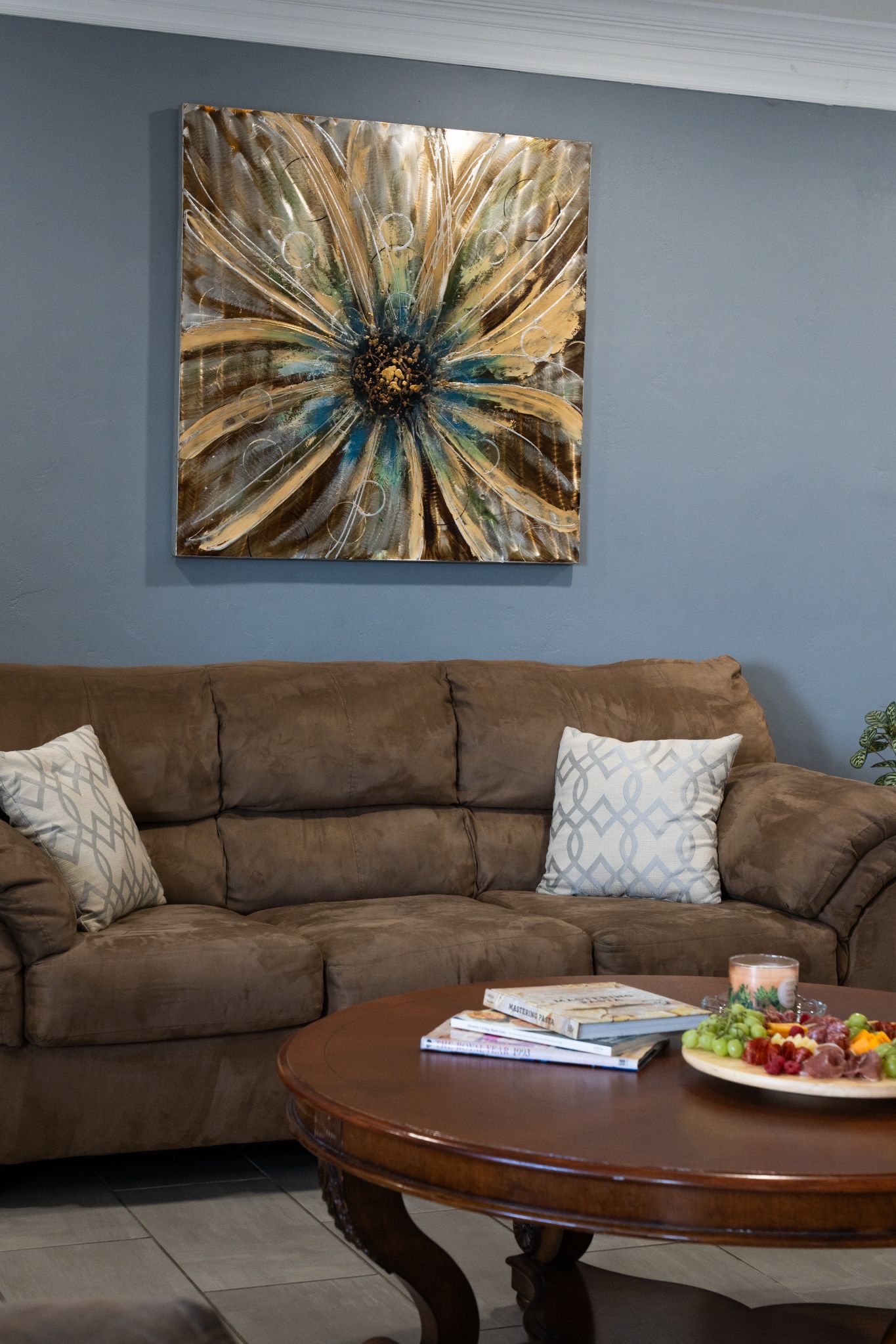 Una sala de estar con un sofá marrón, una mesa de centro con libros y aperitivos, y un cuadro abstracto grande en la pared.