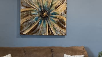 Una sala de estar con un sofá marrón, una mesa de centro con libros y aperitivos, y un cuadro abstracto grande en la pared.