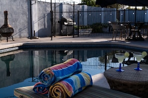 Une piscine avec un bord carrelé, un espace détente avec des meubles en osier et un coin bar doté d’une table en verre et de tabourets de bar.
