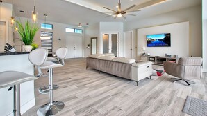 A modern living room with a sofa, a TV, and a ceiling fan. - Elegant Modern Home on Salt Water Canal w/ Heated Pool (Cape Coral)
