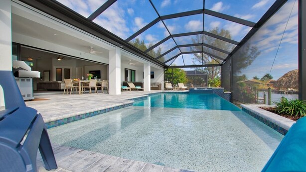 A covered swimming pool with a patio area, a dining setup, and a view of a body of water. - Elegant Modern Home on Salt Water Canal w/ Heated Pool (Cape Coral)