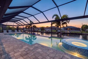A swimming pool with a covered area, lounge chairs, and a view of a marina at sunset.
