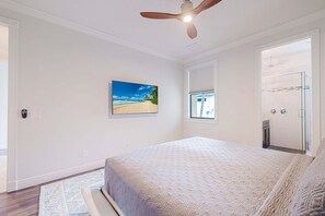 A bedroom with a bed, a ceiling fan, a beach scene painting, and a shower area. - Modern Luxury Waterfront Home W/ Heated Pool (Cape Coral)