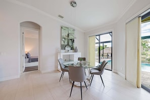 A modern dining area with a glass table and chairs, a cityscape artwork on the wall, and a view of an outdoor pool area.