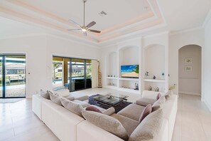Een ruime woonkamer met een grote witte bank, een flatscreen-televisie en een plafondventilator.
