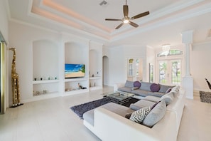 A spacious living room with a white sofa, a glass coffee table, and a ceiling fan.