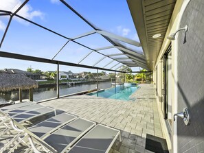 A covered outdoor swimming pool with a glass barrier, lounge chairs, and a view of a marina.