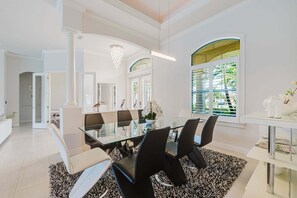 A modern dining area with a glass table, black and white chairs, and a chandelier.