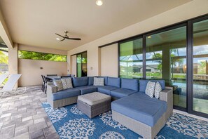A covered outdoor seating area with a sectional sofa, wicker ottomans, and a patterned rug. - Modern Luxury Waterfront Home W/ Heated Pool (Cape Coral)