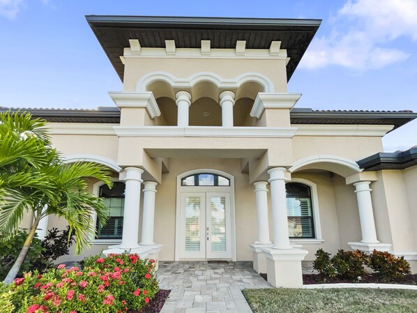 A two-story house with a symmetrical facade, featuring a central entrance with a glass door, flanked by white columns and decorative arches.