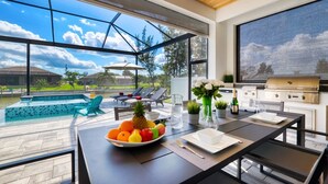 A modern outdoor dining area with a pool view, a grill, and lounge chairs.