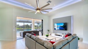A modern living room with a large gray sectional sofa, a flat-screen TV mounted on the wall, and a ceiling fan.