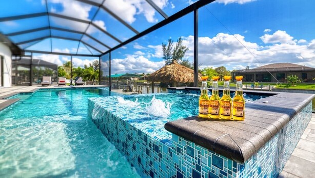 A pool with clear blue water, a tiled edge, and four Corona Light bottles on a ledge.