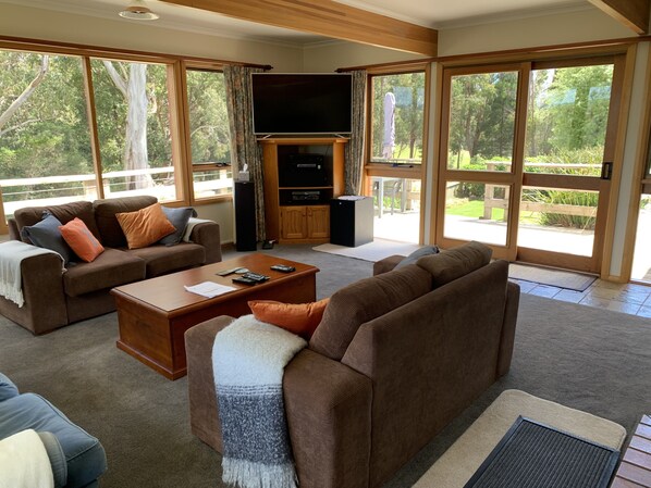 Un salón amplio con una televisión grande, asientos cómodos y vistas al exterior.