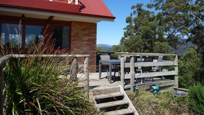 A house with a red roof, brick walls, and a wooden deck with outdoor furniture. - Black Bluff View Retreat - a large comfortable 5 bedroom house on 40 hectares. (North Motton)