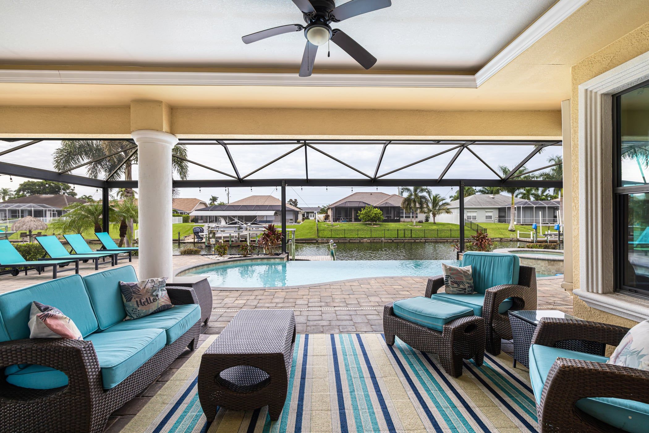 A covered outdoor area with a pool, lounge chairs, and a ceiling fan.