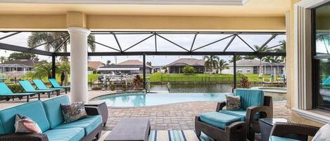 A covered outdoor area with a pool, lounge chairs, and a ceiling fan.