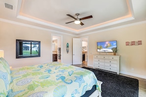 A bedroom with a bed, a ceiling fan, a television, and a door leading to another room. - Sunset Views Over Infinity Pool w/ Boat Dock (Cape Coral)