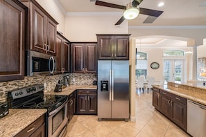 A modern kitchen with dark wood cabinets, stainless steel appliances, and a granite countertop. - Sunset Views Over Infinity Pool w/ Boat Dock (Cape Coral)