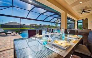 Un espace de restauration en plein air avec une table en verre, des chaises et une vue sur une piscine et des maisons.