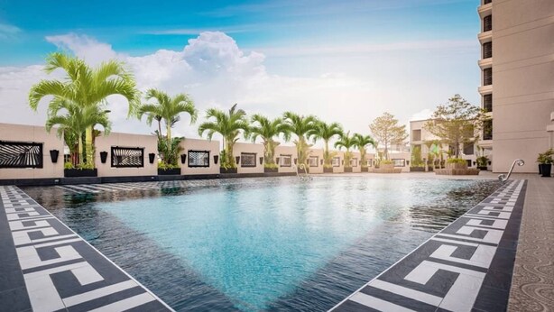 A swimming pool with a geometric tile pattern, surrounded by palm trees and modern buildings.