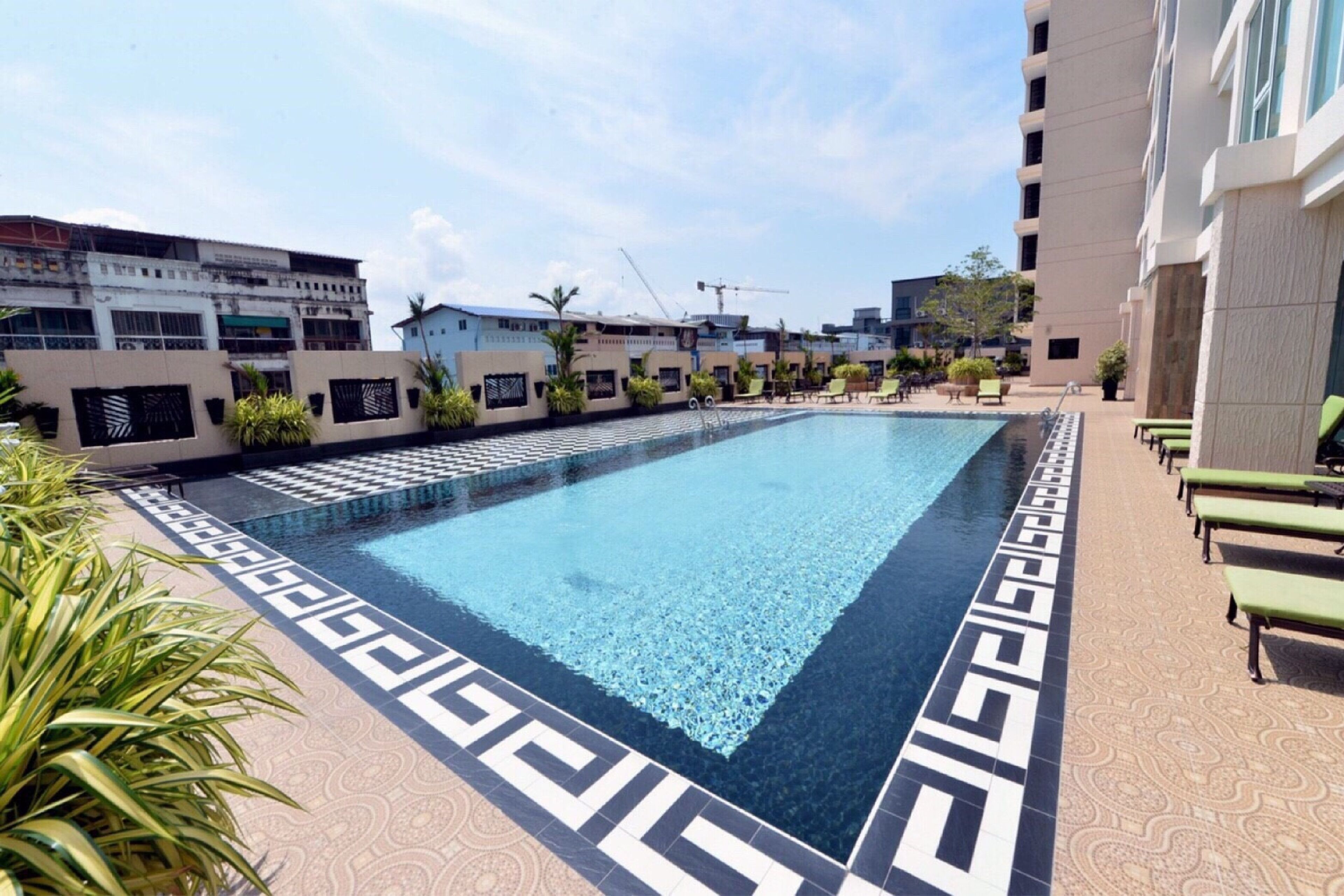 Une piscine dont le carrelage présente un motif géométrique, entourée de chaises longues et de plantes en pot.